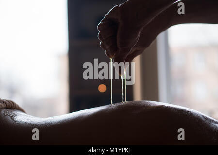 Masseur Pours Warm oil on the Back of Young Girl Receiving Relaxing Body Massage Stock Photo