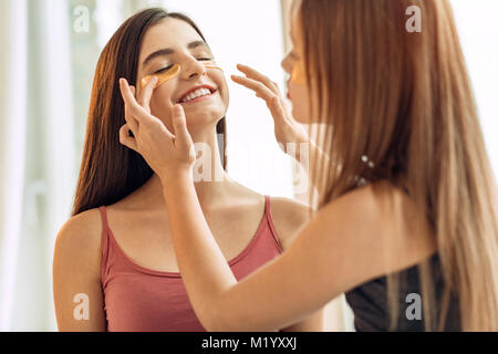 Caring girl adjusting under-eye patches on sisters face Stock Photo