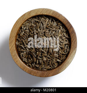 Dry caraway or cumin seeds in dark wood bowl isolated on white from above. Stock Photo