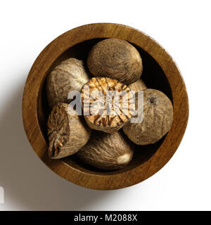 Dried whole and cut nutmegs in dark wood bowl isolated on white from above. Stock Photo