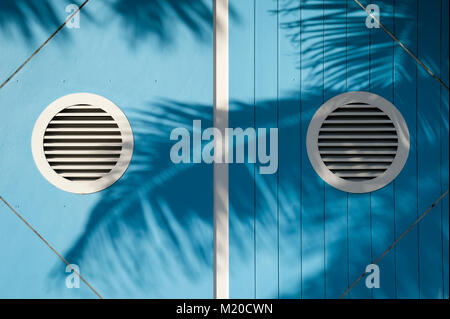 Textured background of tropical palm frond shadows waving in bright sun across bright blue nautical-theme wall Stock Photo