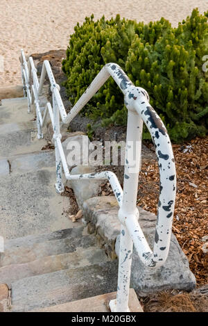 Top view of stairs leading to sandy beach, Sydney, Australia. Steep staircase, old white rusty rail to sand with footsteps. Stock Photo