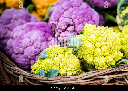 Colorful organic fresh vegetables in wooden boxes displayed at market. Vivid green romanesco broccoli, purple and orange cauliflower at market stall. Stock Photo