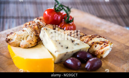 Cheese platter, antipasto, marinated olives, tomatoes and crackers on wooden board, closeup. Delicious fresh cheese variety, cheese sticks, food macro Stock Photo