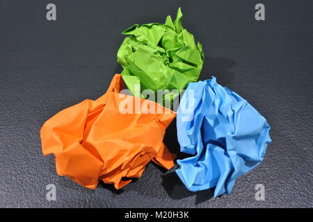 A vibrant display of creativity: three crumpled paper balls in orange, light green, and light blue, artfully arranged in a triangular formation on a t Stock Photo