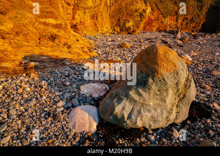 Golden cliffs, pebbles and rocks at Church Bay, Anglesey, Wales in summer sunshine Stock Photo