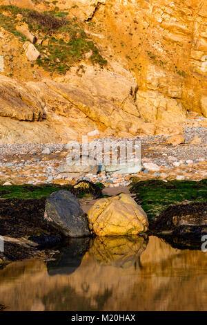 Rocks and cliffs reflecting in a tidal pool on the coast of Anglesey, North Wales Stock Photo