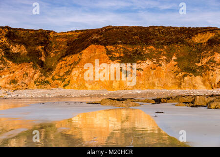 Cliffs reflecting in wet sand on the coast of Anglesey Stock Photo