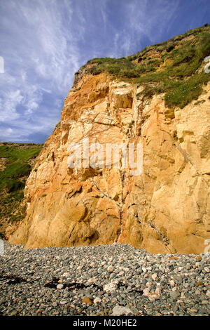 Colourful rocks, pebbles and cliff under blue skies at Church Bay, Anglesey, North Wales Stock Photo