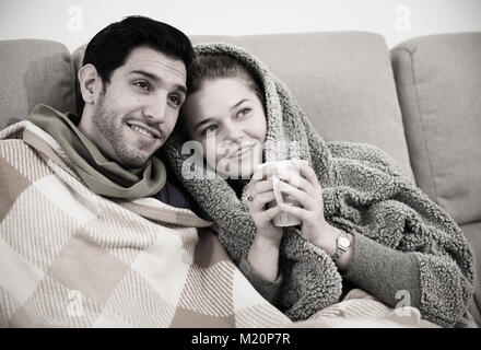 Young couple relaxing together, lying on sofa under blanket watching TV Stock Photo