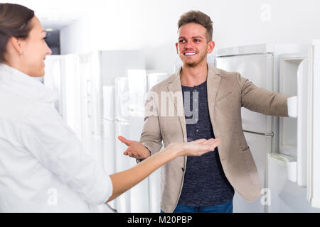Smiling shop assistant helps woman to choose fridge in the shop Stock Photo