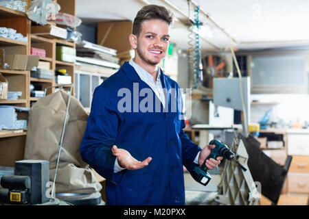 Young cheerful positive male worker using drill for work at workshop Stock Photo