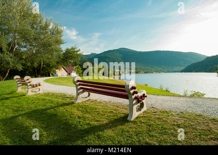 Nelson, British Columbia, Canada.  Two sunlit park benches beside a curved gravel path overlook Kootenay Lake from Rotary Lakeside Park. Stock Photo