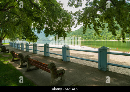 Nelson, British Columbia, Canada.  Two park benches in tree shade beside a concrete sidewalk in Rotary Lakeside Park. Stock Photo