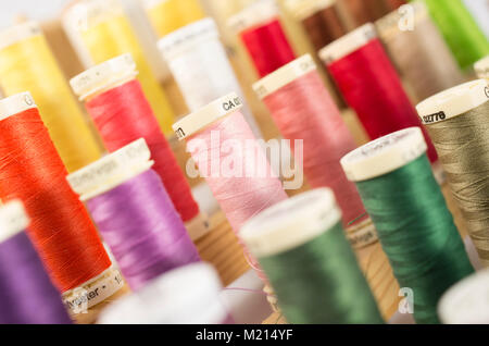 Plastic spools of thread of a variety of colors tilted at an angle and arranged diagonally in rows on a wooden rack Stock Photo