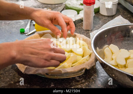 Homemade apple pie in a glass pan on a countertop being prepared by a woman putting slices into the lower crust Stock Photo