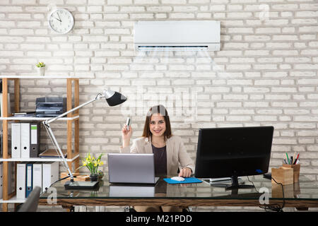 Young Businesswoman Operating Air Conditioner With Remote Controller In Office Stock Photo