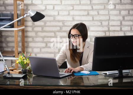 Young Smiling Young Businesswoman With Eyeglasses Using Computer In Office Stock Photo