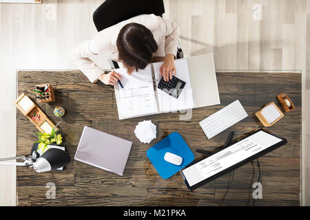 Elevated View Of A Businesswoman Calculating Invoice At Workplace Stock Photo