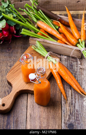 Freshly squeezed carrot juice and organic raw vegetables over rustic wooden table, harvest time Stock Photo