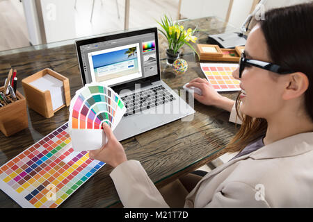 A Female Designer Using Laptop While Holding Colour Swatches In Her Hand Stock Photo