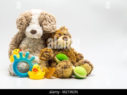 2 plush brown teddy bears with a baby rattle, teething ring, pacifier and 2 rubber ducks isolated on a solid background Stock Photo