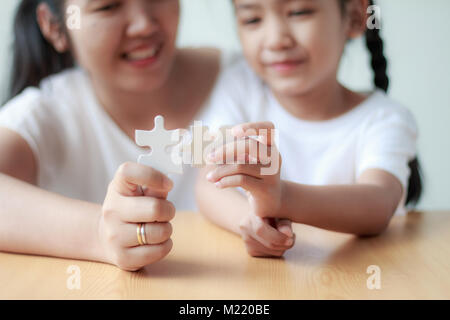 Asian little girl playing jigsaw puzzle with her mother for family concept shallow depth of field select focus on hands Stock Photo