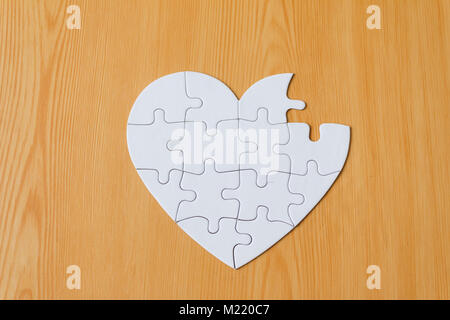 Incomplete heart shape jigsaw puzzle on wooden background Stock Photo
