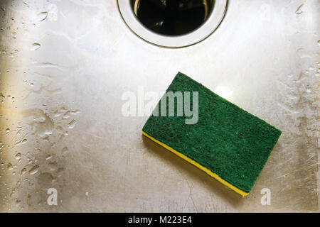 Green and yellow scrubing sponge lying in scratch and wet sink with garage disposal Stock Photo