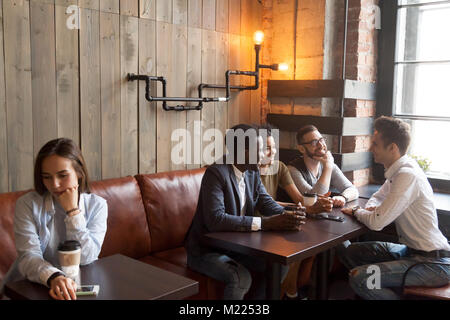 Diverse young friends ignoring sad girl sitting alone in cafe Stock Photo