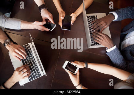 Diverse multiracial people using laptops smartphones on table, t