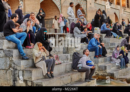 Isfahan, Iran - April 24, 2017: Many people meet sunset sitting on steps of ancient bridge. Stock Photo