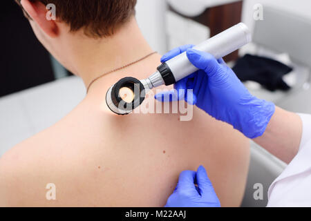 the doctor dermatologist examines birthmarks and birthmarks of the patient with a dermatoscope Stock Photo