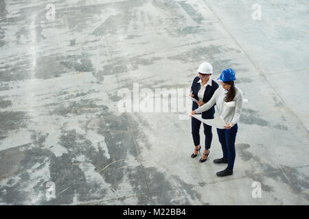 High angle view of two female engineers wearing hardhats examining floor plans in workshop of modern factory, copy space Stock Photo