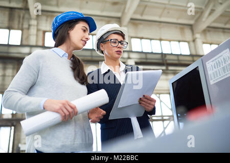 Portrait of two female engineers wearing hardhats standing in  workshop of modern plant holding construction plans Stock Photo