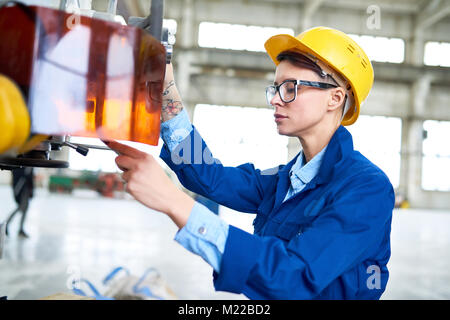 Side view portrait of female factory worker pushing buttons on control panel while working at modern plant Stock Photo