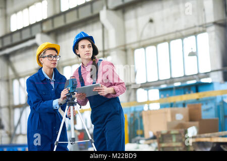 Portrait of two modern young women wearing hardhats setting up optical level mounted on tripod at construction site, copy space Stock Photo
