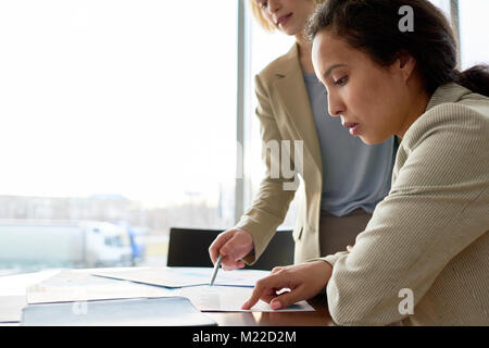 Profile view of concentrated mixed race manager analyzing financial figures while having working meeting with female colleague at spacious boardroom Stock Photo