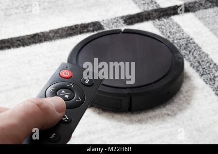 Robotic vacuum cleaner working on carpet. Hand holding remote control Stock Photo