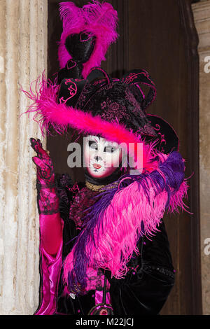 Cat mask - Female Venetian Mask in pink / black elegant costume on St. Mark's Square in Venice with traditional venetian pillar - Venice Carnival Stock Photo