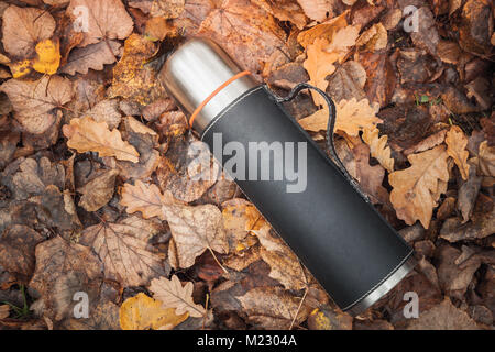 Vacuum thermos made of stainless steel lays on fallen autumn leaves in park Stock Photo