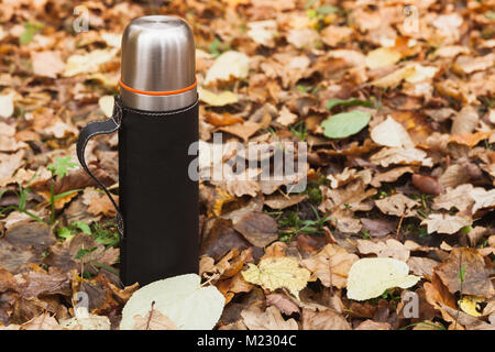 Vacuum thermos made of stainless steel stands on fallen autumn leaves in park Stock Photo