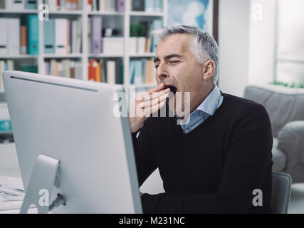 Tired sleepy businessman working at office desk, he is bored and yawning Stock Photo