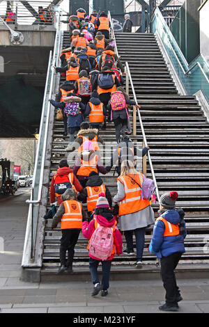 Group of primary school children in high visibility vests with teachers & assistants climbing steep steps onto footbridge crossing River Thames UK Stock Photo