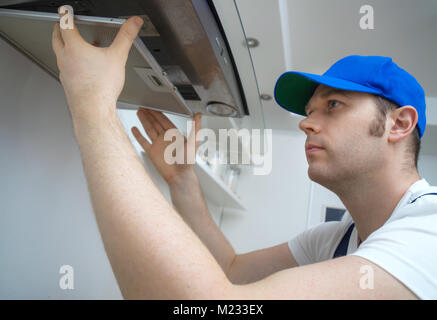Handsome foreman fixing exhaust hood in the kitchen. Stock Photo
