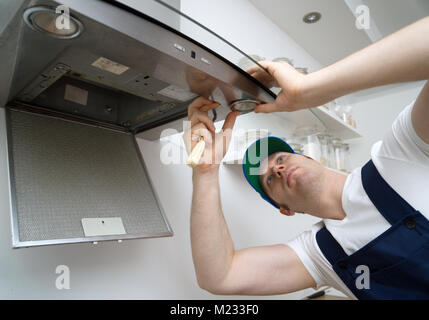 Handsome foreman fixing exhaust hood in the kitchen. Changes the light bulb. Stock Photo