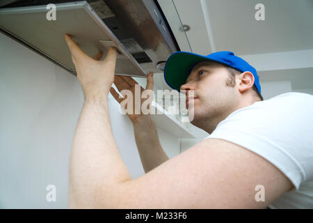 Handsome foreman fixing exhaust hood in the kitchen. Stock Photo