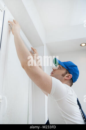 Handsome handyman installing cassette roller blinds. Stock Photo