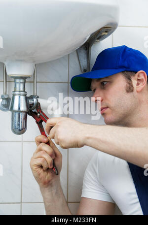 Plumber in uniform repairing old pipeline in the house. Stock Photo