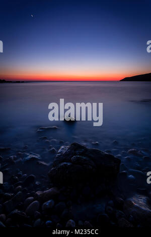 Calm sea and rocks at dusk on the coast of Anglesey, North Wales Stock Photo